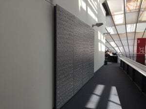 A large grey panel with decorating resembling writing hanging on a top floor library wall
